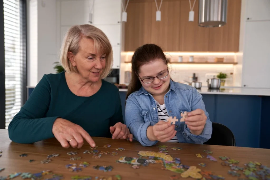 Happy disabled girl with down syndrome sitting at table with support worker completing a puzzle